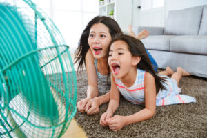 扇風機の前に寝そべって楽しそうに口を開ける母と子