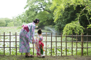 浴衣を着た女性と女の子の親子が、緑に囲まれた池を眺めている