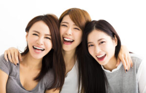 アジア人女性三人が肩を寄せて笑顔をこちらに向けている